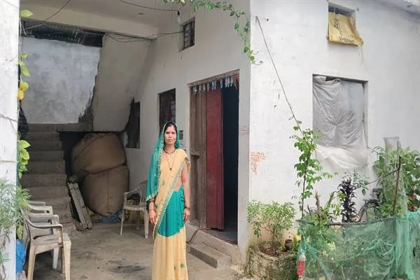 पक्के मकान के प्रवेश द्वार के सामने खड़ी हरे और हल्के पीले रंग की साड़ी पहने महिला