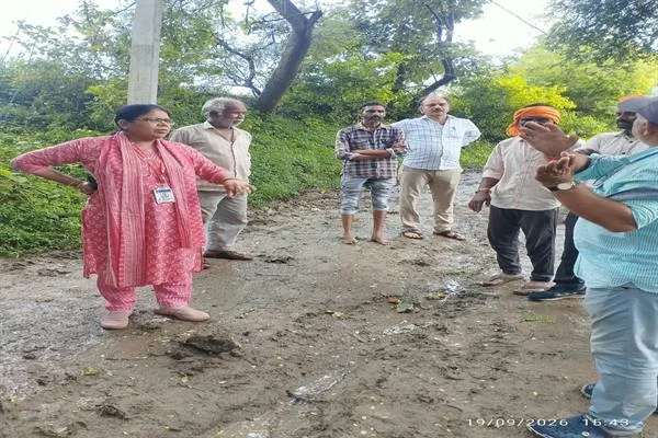 कच्ची और कीचड़ वाली सड़क पर खड़े होकर चर्चा करते महिला अधिकारी और ग्रामीण
