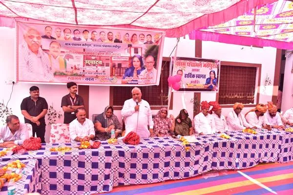 सजे हुए पंडाल में मंच पर माइक से संबोधित करता व्यक्ति और लंबी मेज के पीछे बैठे अतिथि